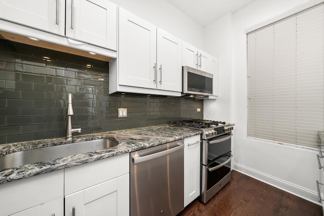 kitchen with stainless steel appliances, a sink, dark wood-type flooring, white cabinetry, and tasteful backsplash