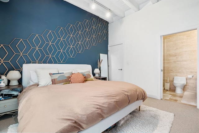 carpeted bedroom featuring track lighting, an accent wall, beam ceiling, and connected bathroom