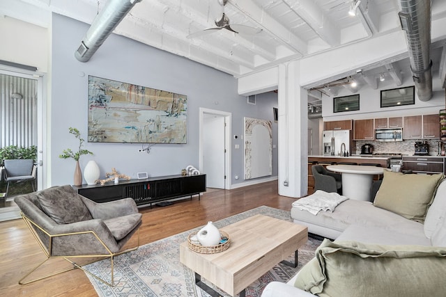 living room with a ceiling fan, wood finished floors, beamed ceiling, a towering ceiling, and rail lighting