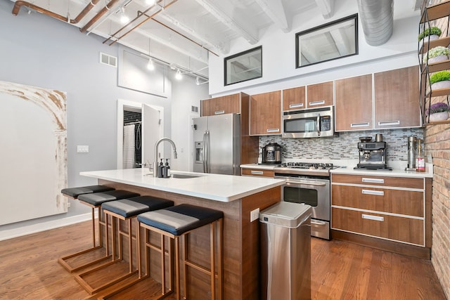 kitchen with stainless steel appliances, a sink, dark wood finished floors, brown cabinetry, and a towering ceiling