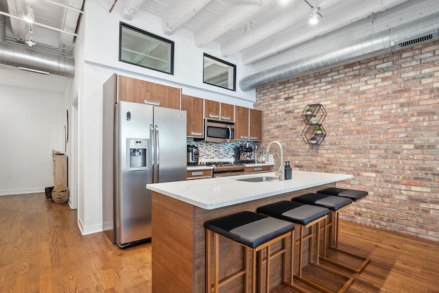 kitchen with a sink, stainless steel appliances, brown cabinets, brick wall, and a high ceiling