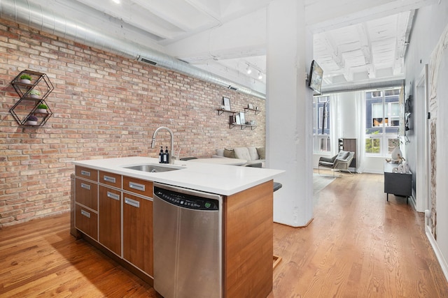kitchen with dishwasher, a sink, brick wall, light wood-style flooring, and light countertops