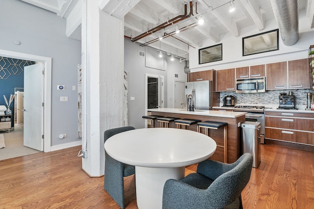kitchen featuring appliances with stainless steel finishes, a kitchen island with sink, track lighting, light countertops, and wood finished floors