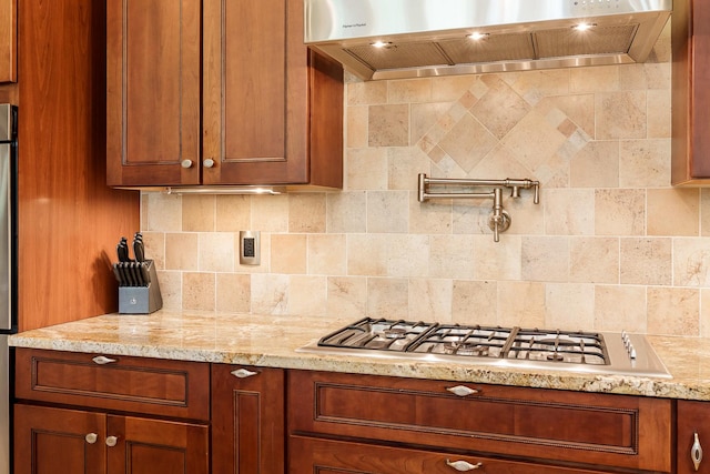 5344 River Run Parkway, Belvidere, IL 61008 - kitchen featuring premium range hood, decorative backsplash, stainless steel gas cooktop, brown cabinetry, and light stone counters