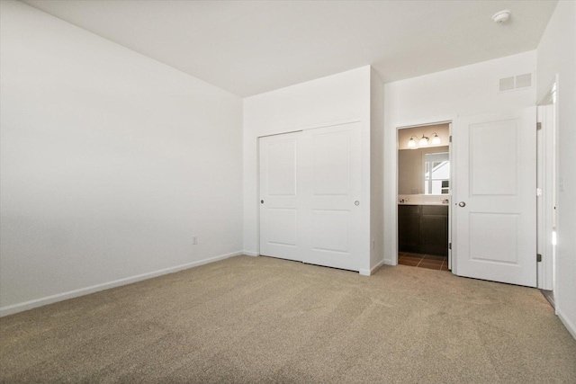 unfurnished bedroom featuring light carpet, baseboards, and ensuite bath