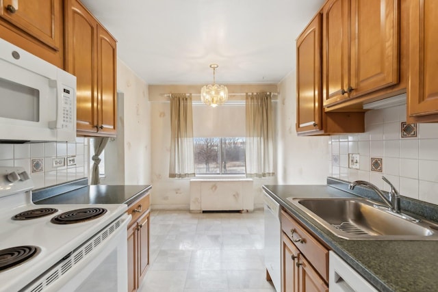 kitchen featuring white appliances, a sink, a chandelier, brown cabinets, and dark countertops
