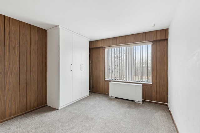 unfurnished bedroom featuring radiator, carpet floors, a closet, and wooden walls
