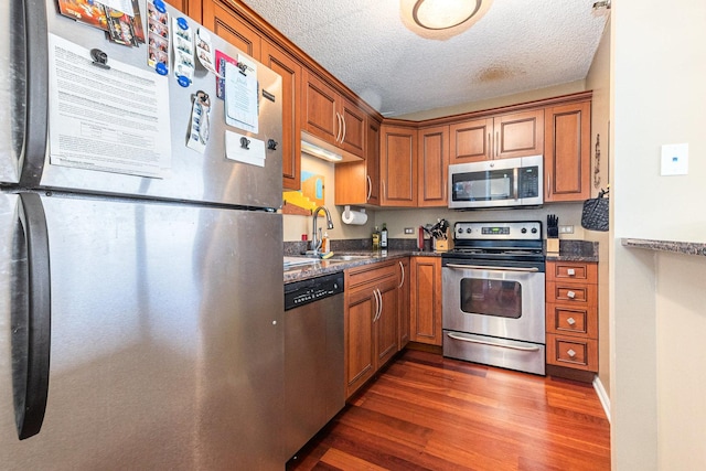 kitchen with stainless steel appliances, a sink, dark wood-style floors, brown cabinetry, and a textured ceiling