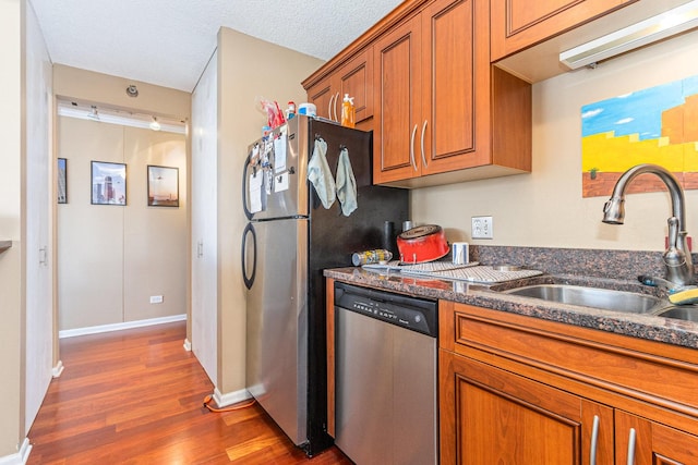 kitchen with appliances with stainless steel finishes, a sink, dark wood finished floors, and brown cabinets