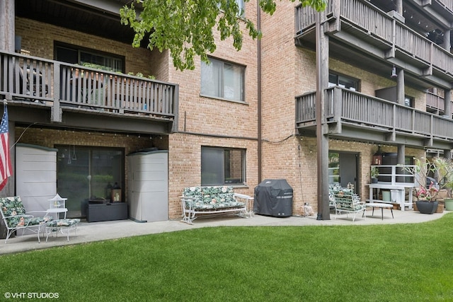exterior space with a balcony, brick siding, a patio area, and a yard