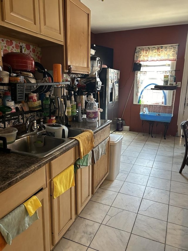 kitchen with stainless steel refrigerator with ice dispenser, dark countertops, a sink, and light tile patterned flooring