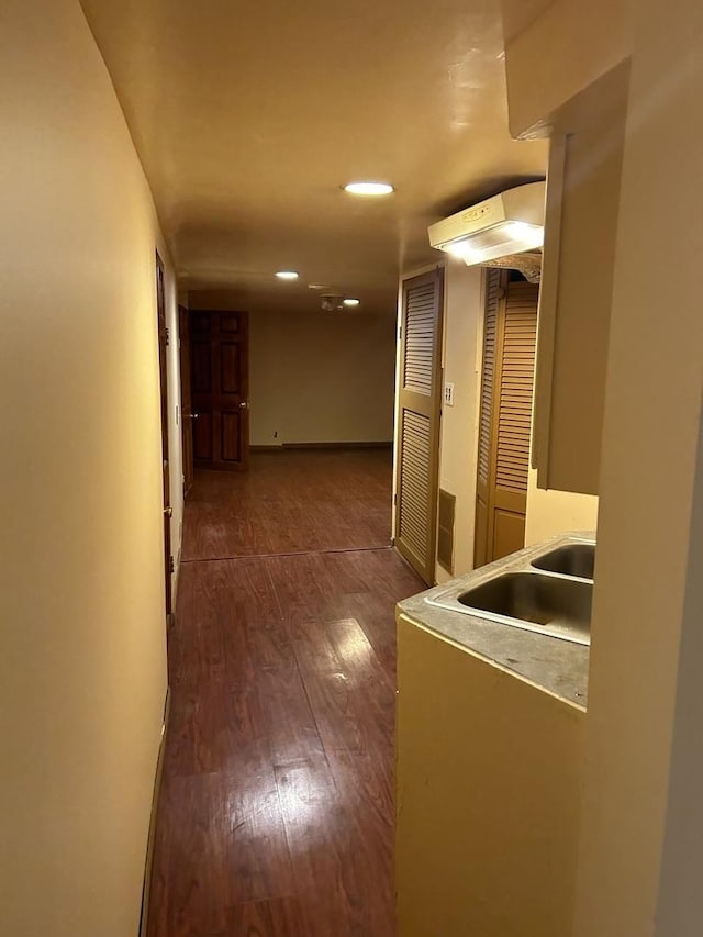 hallway with dark wood-type flooring, recessed lighting, and a sink