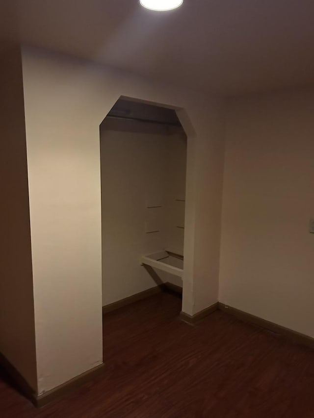 unfurnished room with arched walkways, baseboards, and dark wood-style flooring