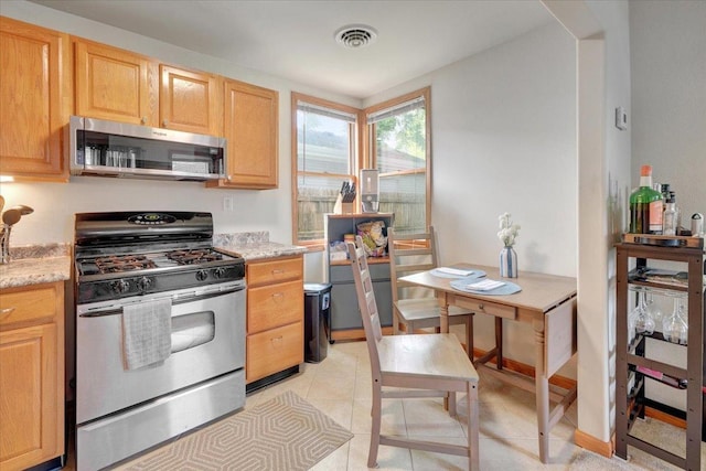 kitchen featuring stainless steel appliances, light brown cabinets, light stone counters, and light tile patterned flooring