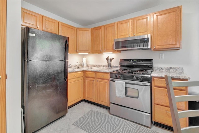 kitchen with appliances with stainless steel finishes, light brown cabinetry, a sink, light tile patterned floors, and light stone counters