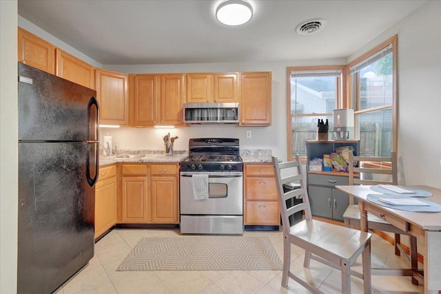 kitchen featuring appliances with stainless steel finishes, light brown cabinetry, light tile patterned floors, and a sink