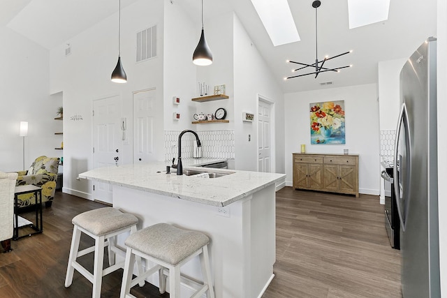 kitchen with a sink, freestanding refrigerator, high vaulted ceiling, a skylight, and dark wood-style floors