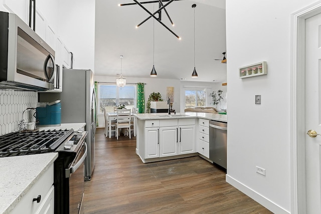 kitchen with appliances with stainless steel finishes, a sink, dark wood-type flooring, white cabinetry, and a chandelier