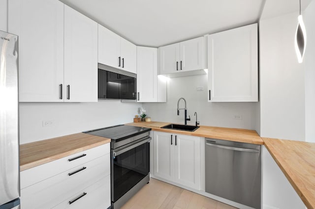 kitchen with wooden counters, stainless steel appliances, a sink, white cabinetry, and light wood-style floors
