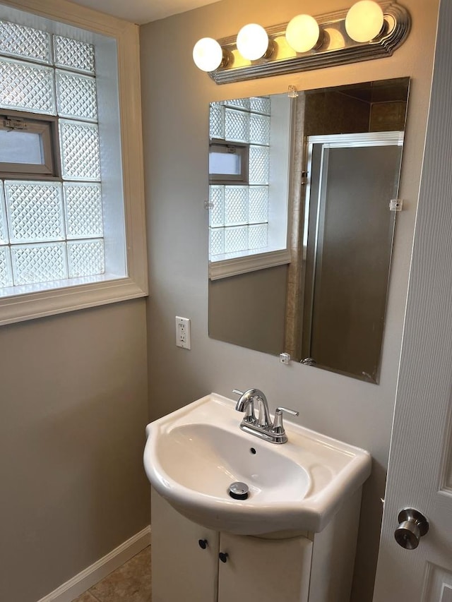 bathroom featuring a stall shower, a sink, and baseboards
