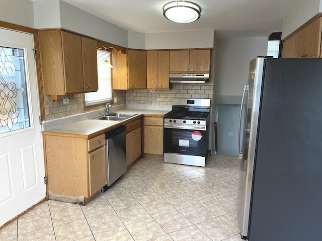 kitchen featuring appliances with stainless steel finishes, under cabinet range hood, a sink, backsplash, and light countertops