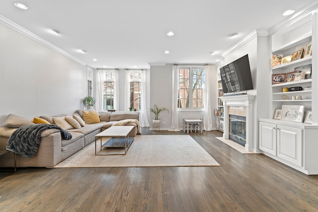 living area with ornamental molding, recessed lighting, a tiled fireplace, wood finished floors, and built in shelves