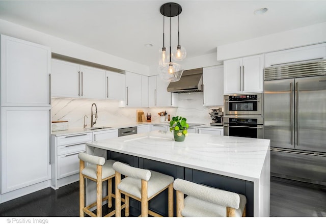 kitchen with stainless steel appliances, a sink, wall chimney exhaust hood, decorative backsplash, and white cabinetry