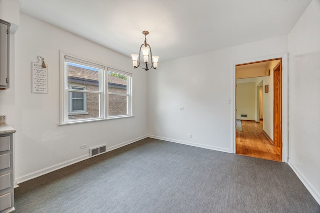 spare room featuring dark carpet, a chandelier, and baseboards