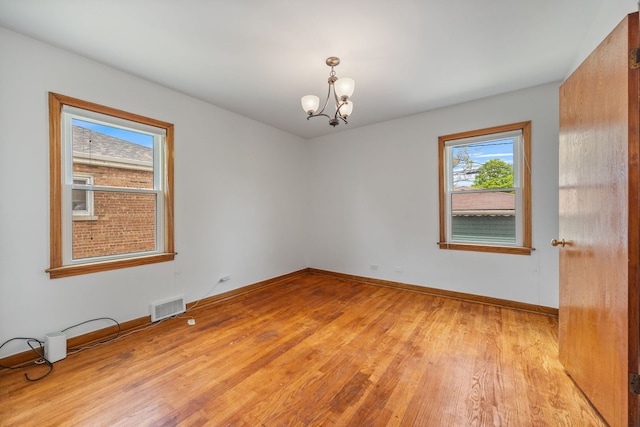 empty room with light wood-style flooring, a chandelier, and baseboards