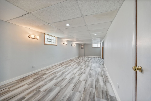 basement with light wood-style flooring, baseboards, plenty of natural light, and a paneled ceiling