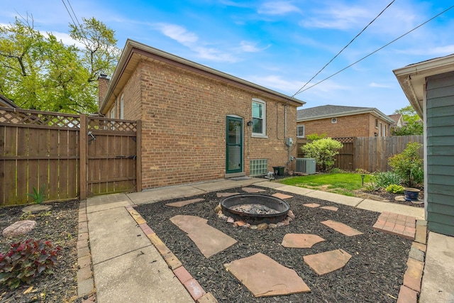 rear view of property featuring an outdoor fire pit, brick siding, central air condition unit, fence, and a gate