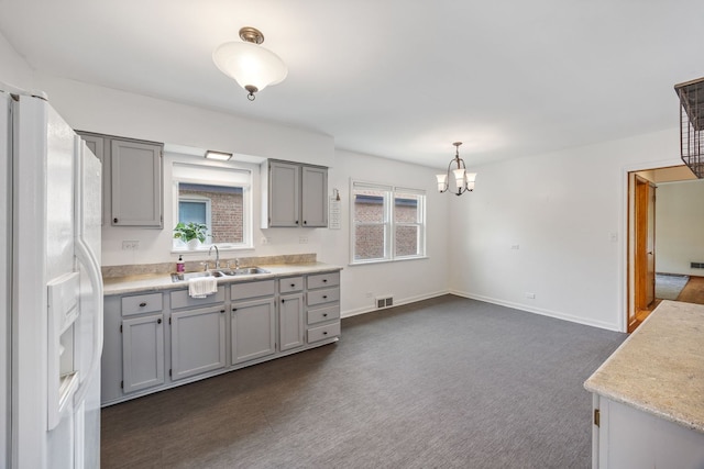 kitchen featuring gray cabinets, white fridge with ice dispenser, a chandelier, and dark carpet