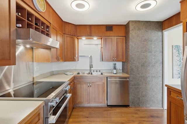 kitchen with appliances with stainless steel finishes, under cabinet range hood, a sink, light countertops, and light wood-type flooring