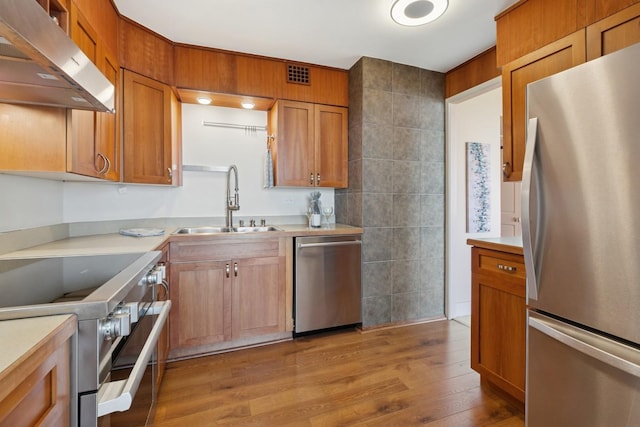 kitchen with stainless steel appliances, under cabinet range hood, a sink, light wood finished floors, and light countertops