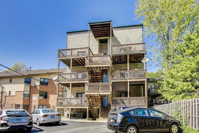 view of building exterior with stairs, uncovered parking, and fence