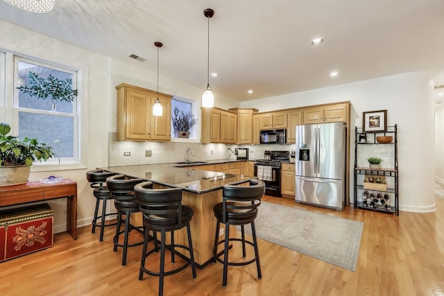 kitchen featuring black appliances, a sink, a peninsula, light wood-type flooring, and decorative backsplash