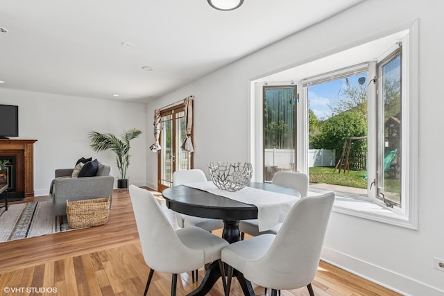 dining space featuring plenty of natural light, baseboards, light wood-style flooring, a glass covered fireplace, and recessed lighting