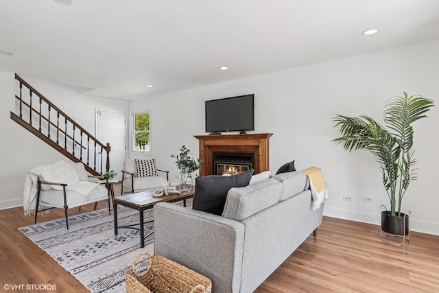 living room featuring light wood finished floors, stairway, baseboards, a glass covered fireplace, and recessed lighting