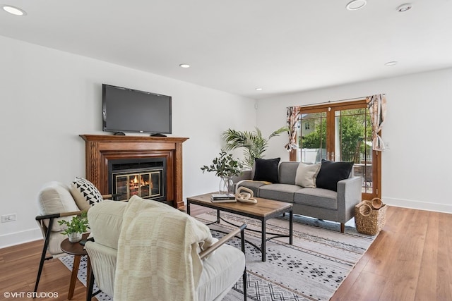 living area featuring wood finished floors, a glass covered fireplace, baseboards, and recessed lighting