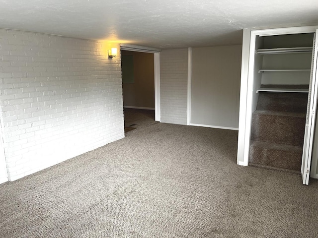 spare room featuring carpet floors, brick wall, and baseboards