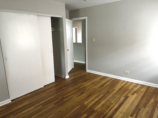 unfurnished bedroom featuring dark wood-style flooring, a closet, and baseboards
