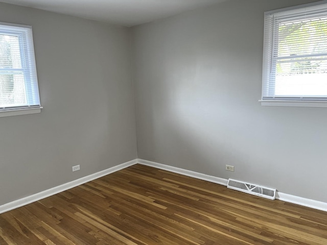 unfurnished room with dark wood finished floors, healthy amount of natural light, and baseboards