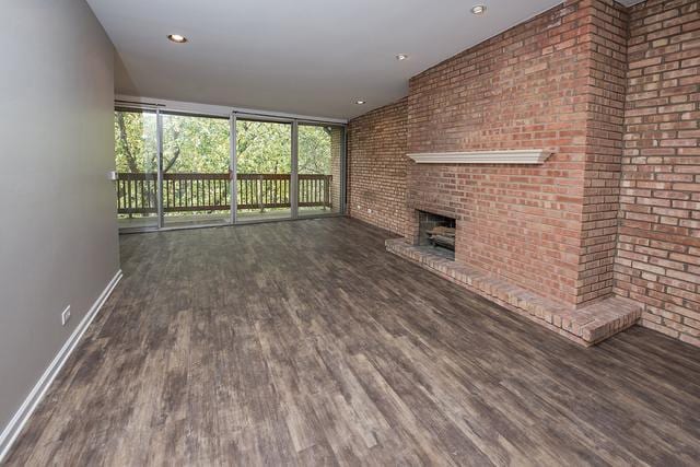 unfurnished living room with wood finished floors, plenty of natural light, a brick fireplace, brick wall, and baseboards