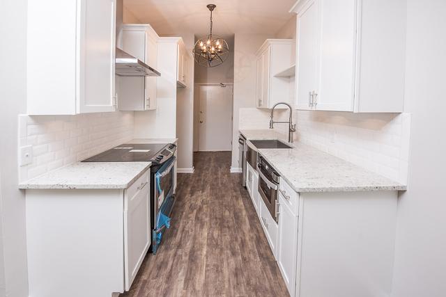 kitchen with stainless steel appliances, wall chimney range hood, tasteful backsplash, a sink, and white cabinets