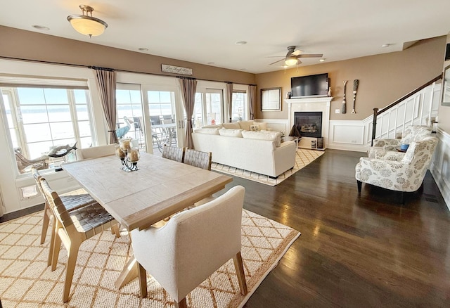 dining space with a ceiling fan, wood finished floors, a glass covered fireplace, and stairs