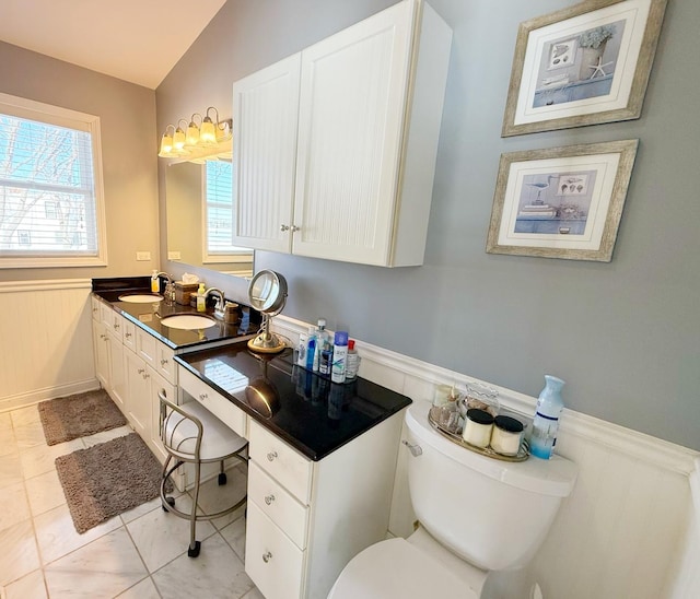 bathroom with a wainscoted wall, toilet, tile patterned flooring, vanity, and lofted ceiling