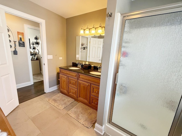 bathroom with a shower stall, double vanity, tile patterned floors, and baseboards