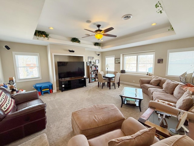 living area with a raised ceiling, light colored carpet, ceiling fan, and baseboards