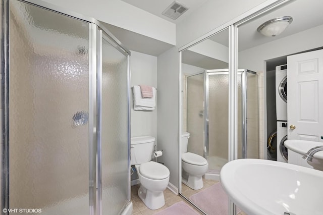 bathroom with stacked washer / dryer, tile patterned flooring, a stall shower, toilet, and a sink