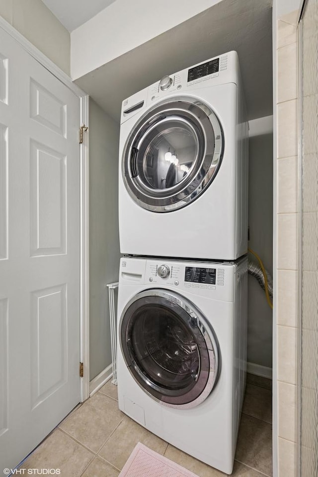 washroom with stacked washer and clothes dryer, light tile patterned floors, and baseboards